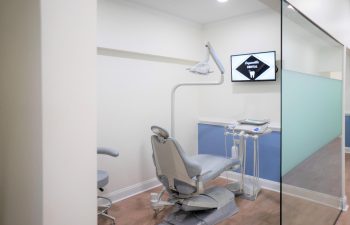 A modern dental examination room with a chair, dental equipment, and a monitor displaying "Welcome to Open smile Dental".