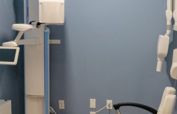 A blue-walled dental examination room featuring an x-ray machine and a white dental chair.