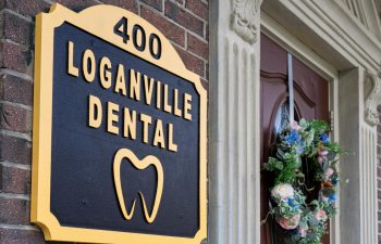 Sign for "Loganville Dental" with a tooth symbol, located at 400, mounted on a brick wall next to a door adorned with a floral wreath.