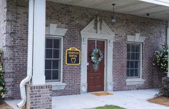 The entrance to Loganville Dental with brown door, decorative wreath, and two windows on either side. A yellow sign above the door reads "400 Loganville Dental.